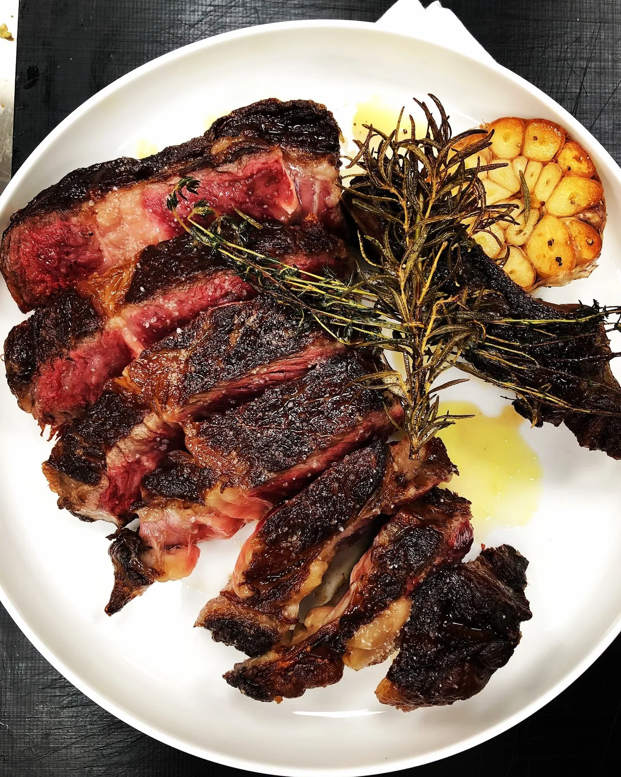 A large grilled rib steak with rosemary and roasted garlic on a white plate