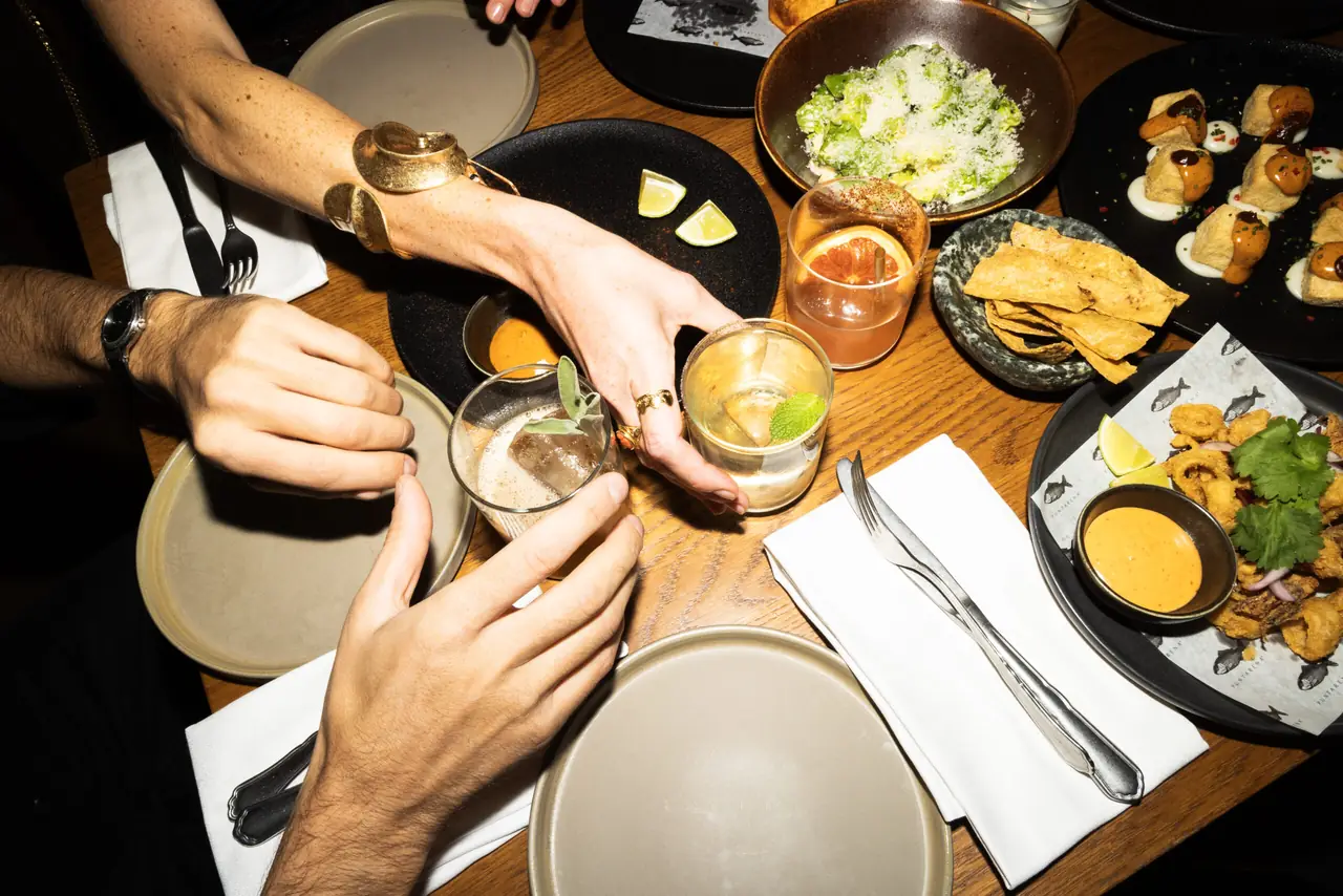 Table spread of cocktails, fried calamari with chipotle aioli, tortilla chips, tostadas and a Caesar salad