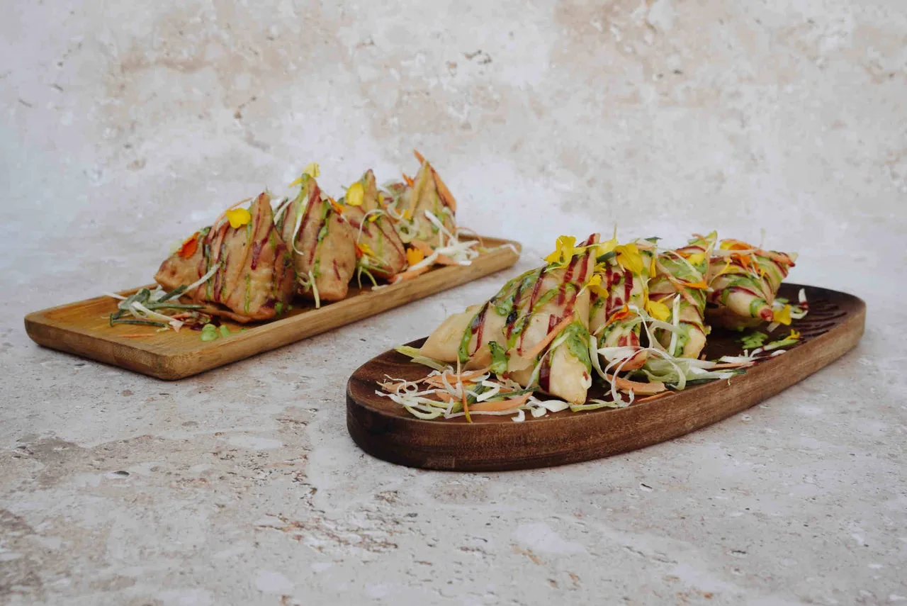 Two wooden boards of triangular pastries topped with green and orange garnish on a stone surface