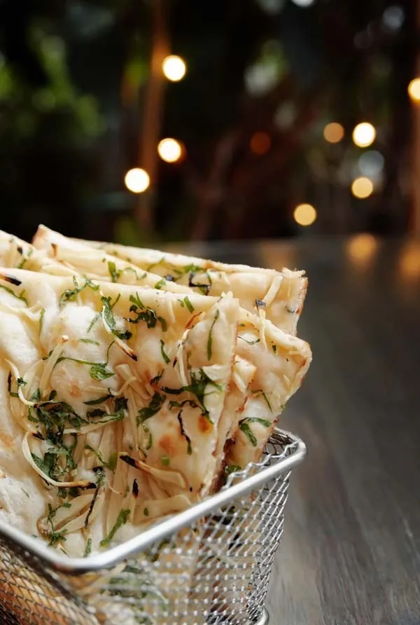 A stack of flatbread cut into triangles in a small metal basket