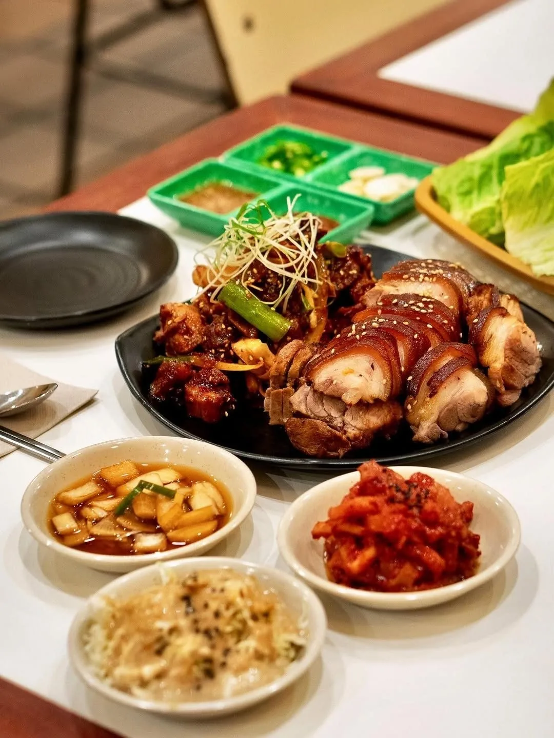 A dark platter of glazed pork trotter with side dishes and lettuce on a table