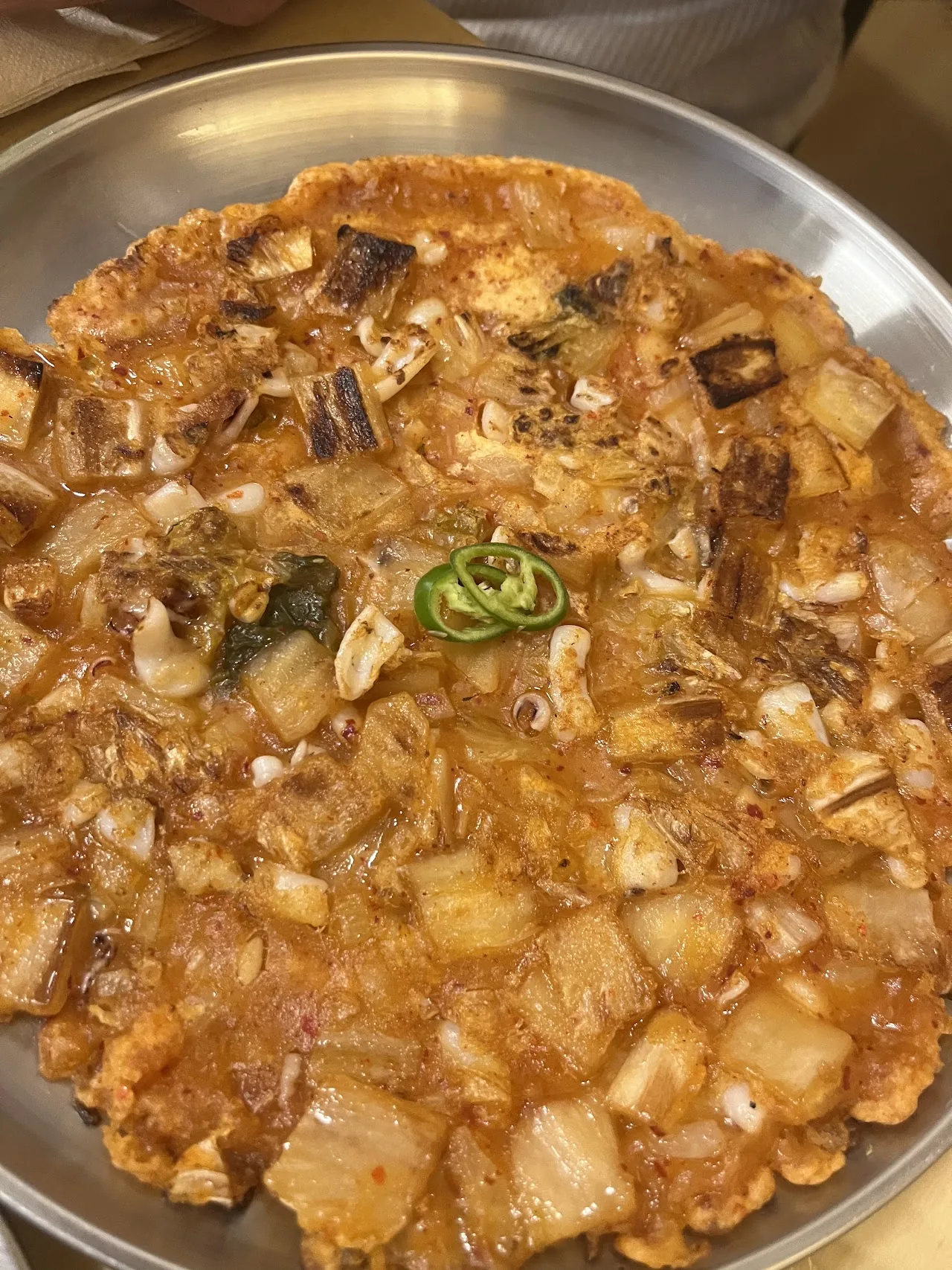 A close-up of a Korean seafood and scallion pancake in a metal pan