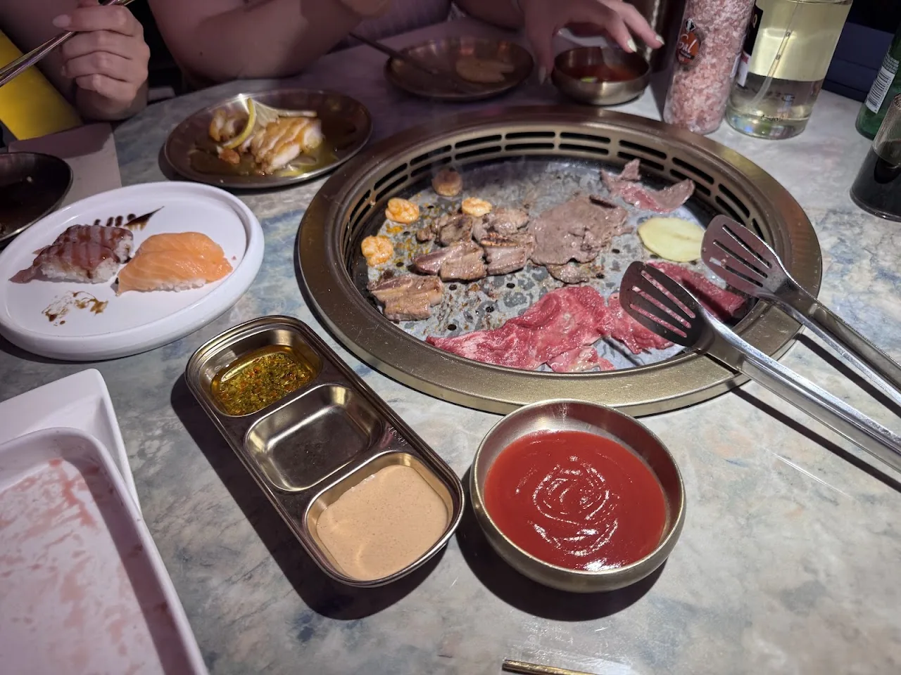 Raw meat cooking on a tabletop grill with dipping sauces