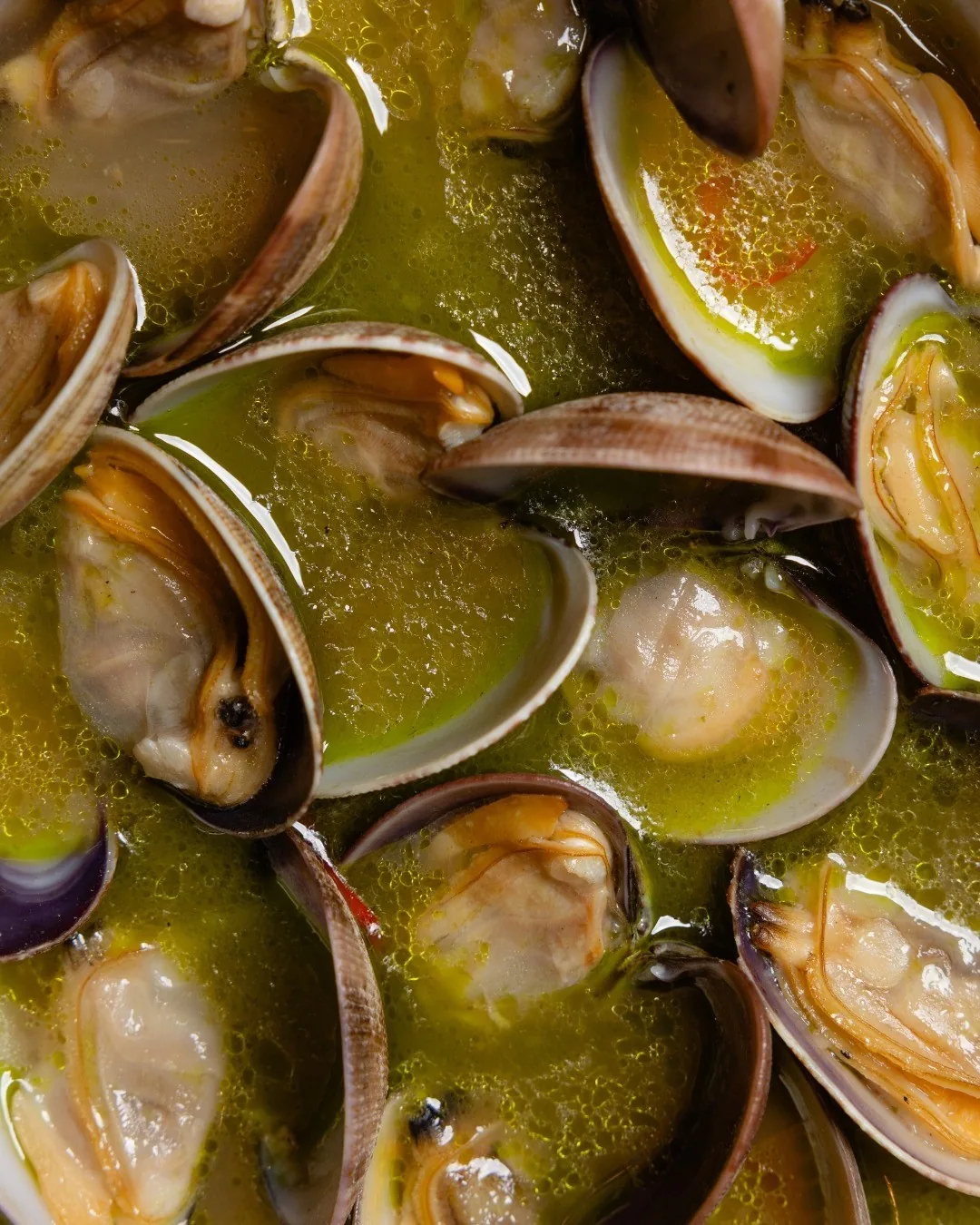 A close view of open clams in a green sauce