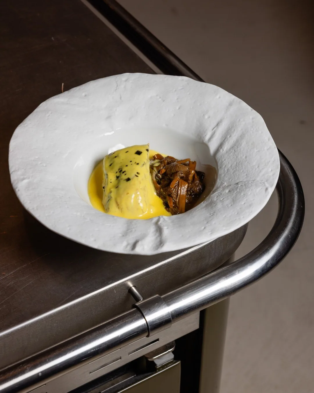 A creamy yellow dish with a piece of meat on a white bowl-shaped plate