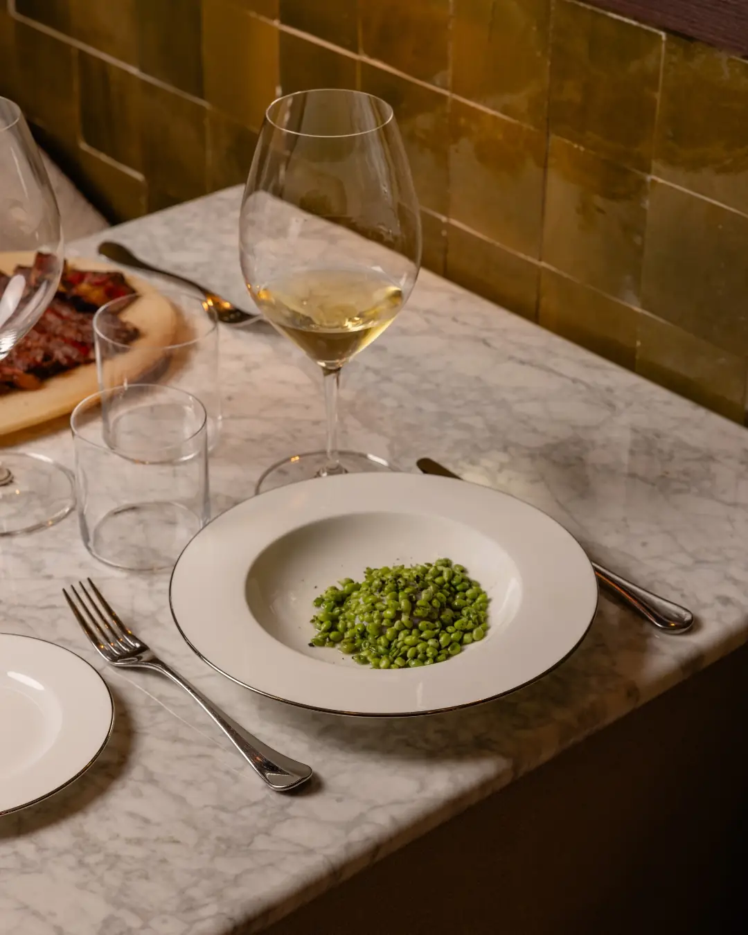 Bowl of dressed green beans with a glass of white wine on a marble table