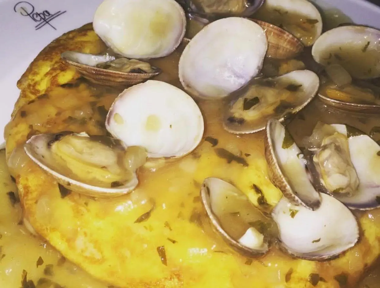 Close-up of clams in a green parsley-garlic sauce over a Spanish omelette on a white plate, with a small faint Pepa signature watermark