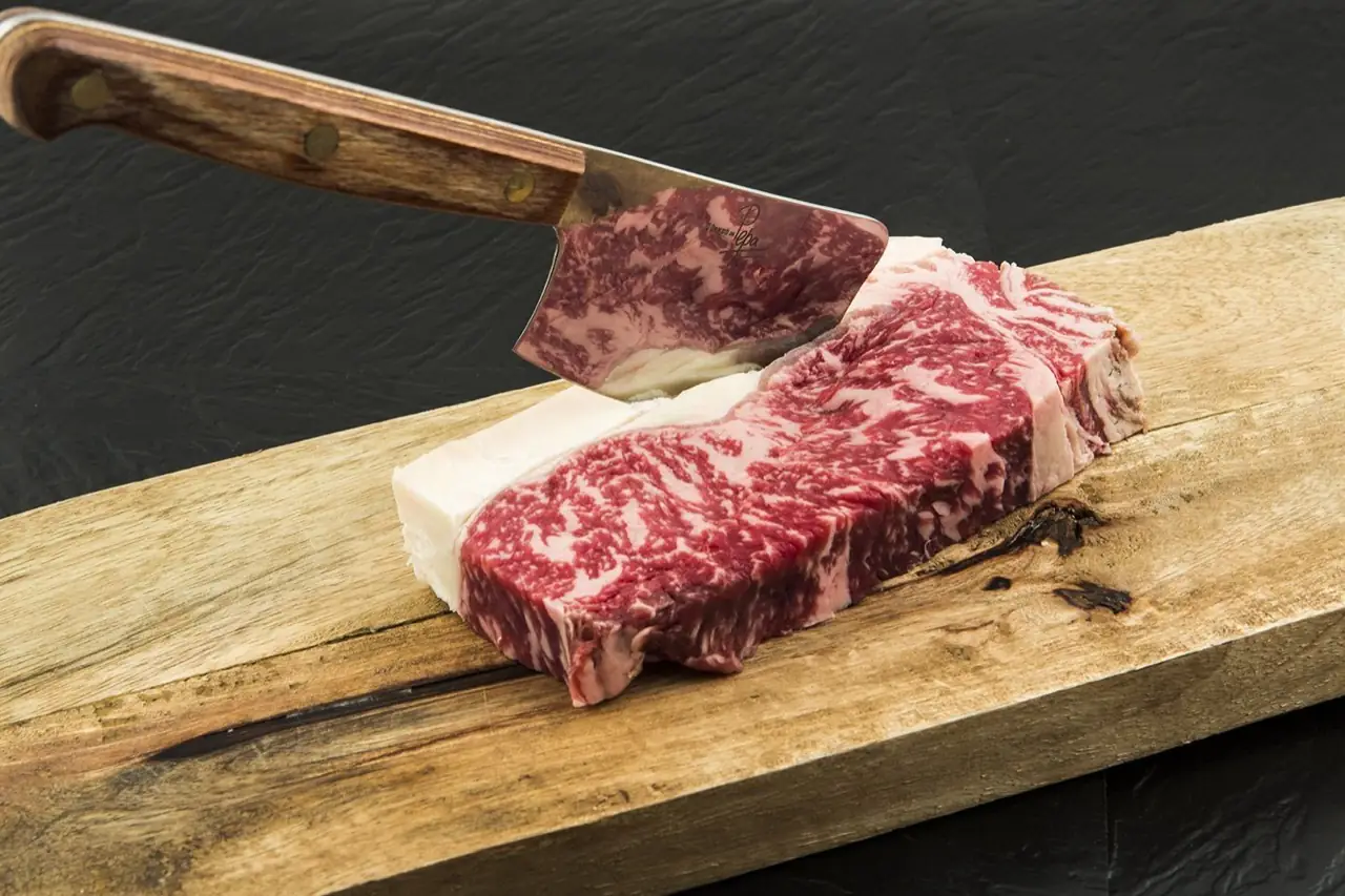 Marbled raw beef sirloin cut on a wooden board with a wood-handled chef's knife resting against it on a dark surface