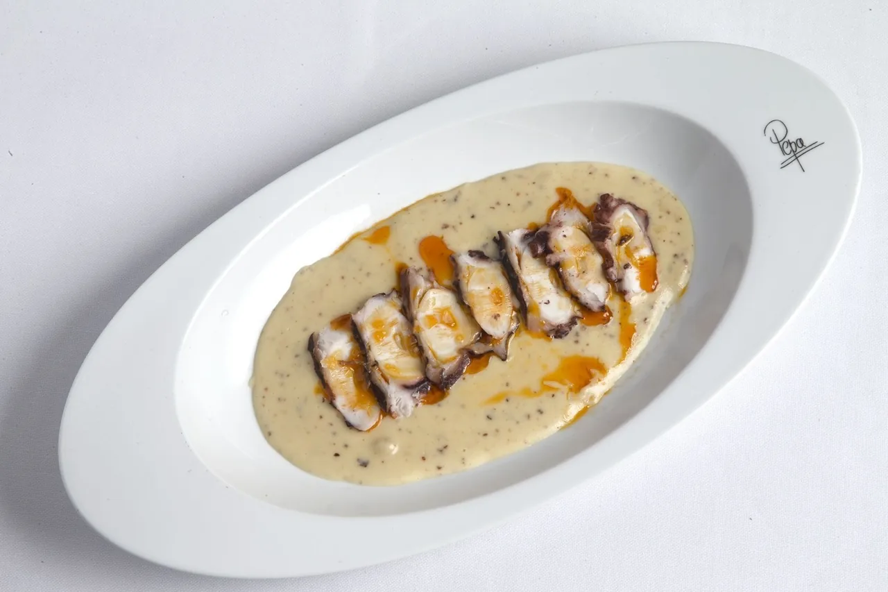 A long white plate of a creamy sauce with small pieces of seafood