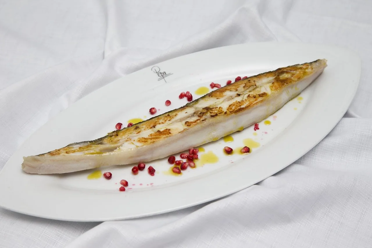A grilled flat fish with pink peppercorns on a white oval plate