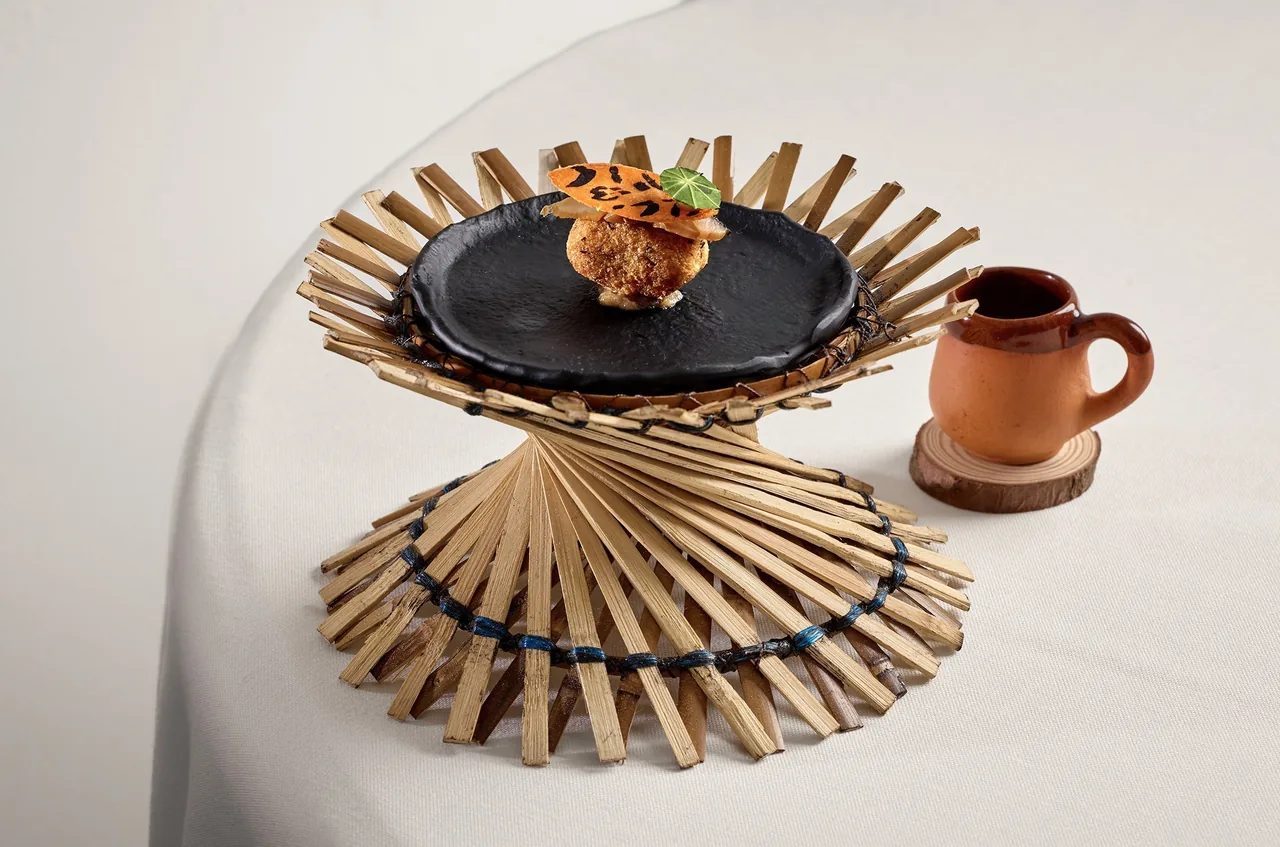 A crisp topped dish on a black plate set on a woven bamboo stand beside a clay mug