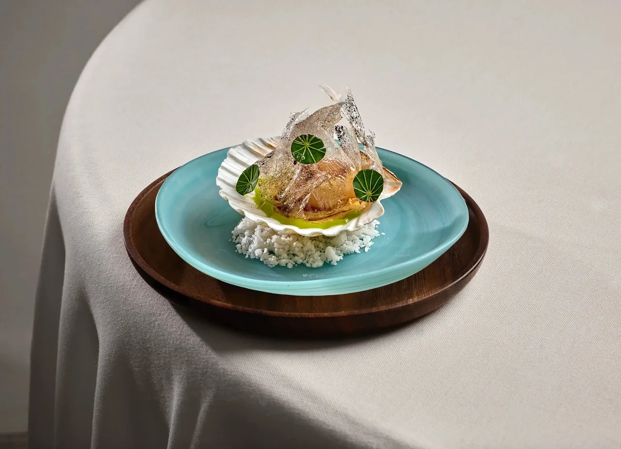 A shell-shaped dish on a turquoise plate with rice and green leaves