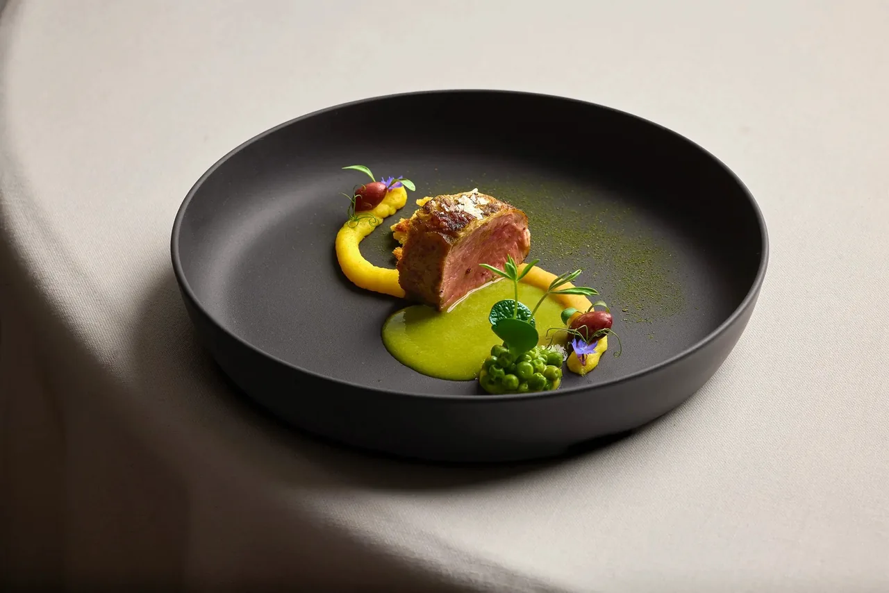 A dark bowl with seared meat and a bright green sauce on a white tablecloth