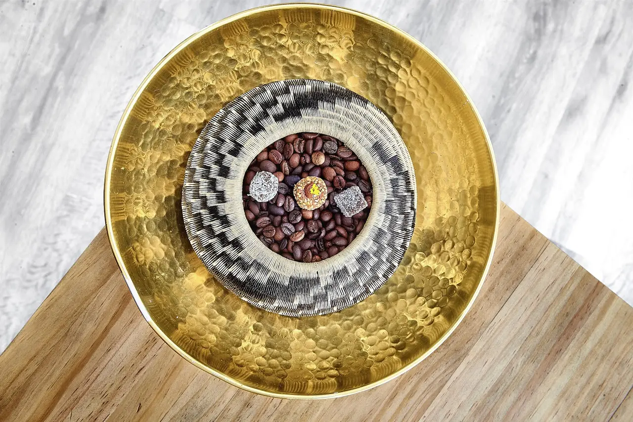 Three small bite-size confections plated in a woven basket nestled in coffee beans, on a gold bowl