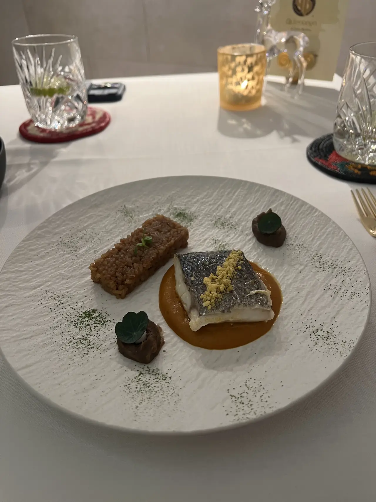 Plated fish fillet with crispy skin over orange sauce, alongside a rice bar and small garnishes