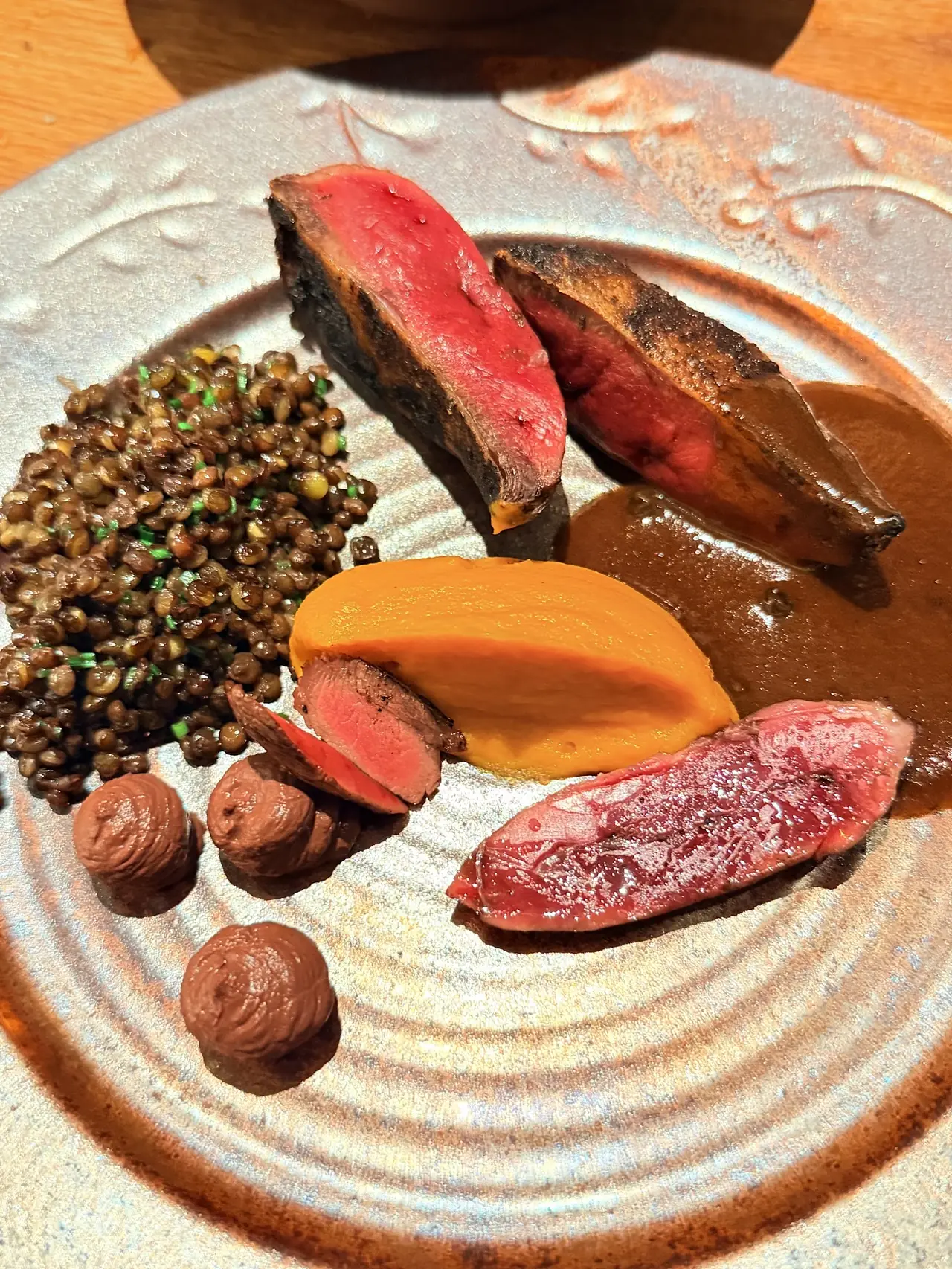 Sliced rare game meat with lentils, chestnuts and squash puree in a rich sauce