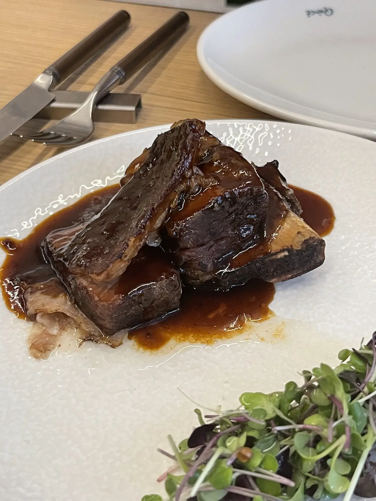 Braised short rib with bone in a glossy sauce, plated with microgreens