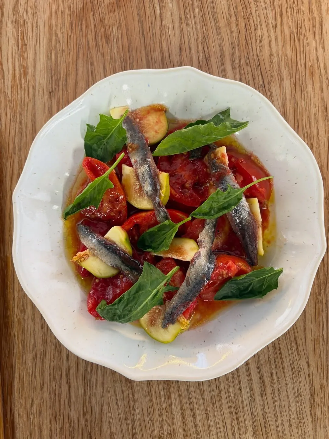A floral rimmed plate of tomato, fish fillets and basil leaves
