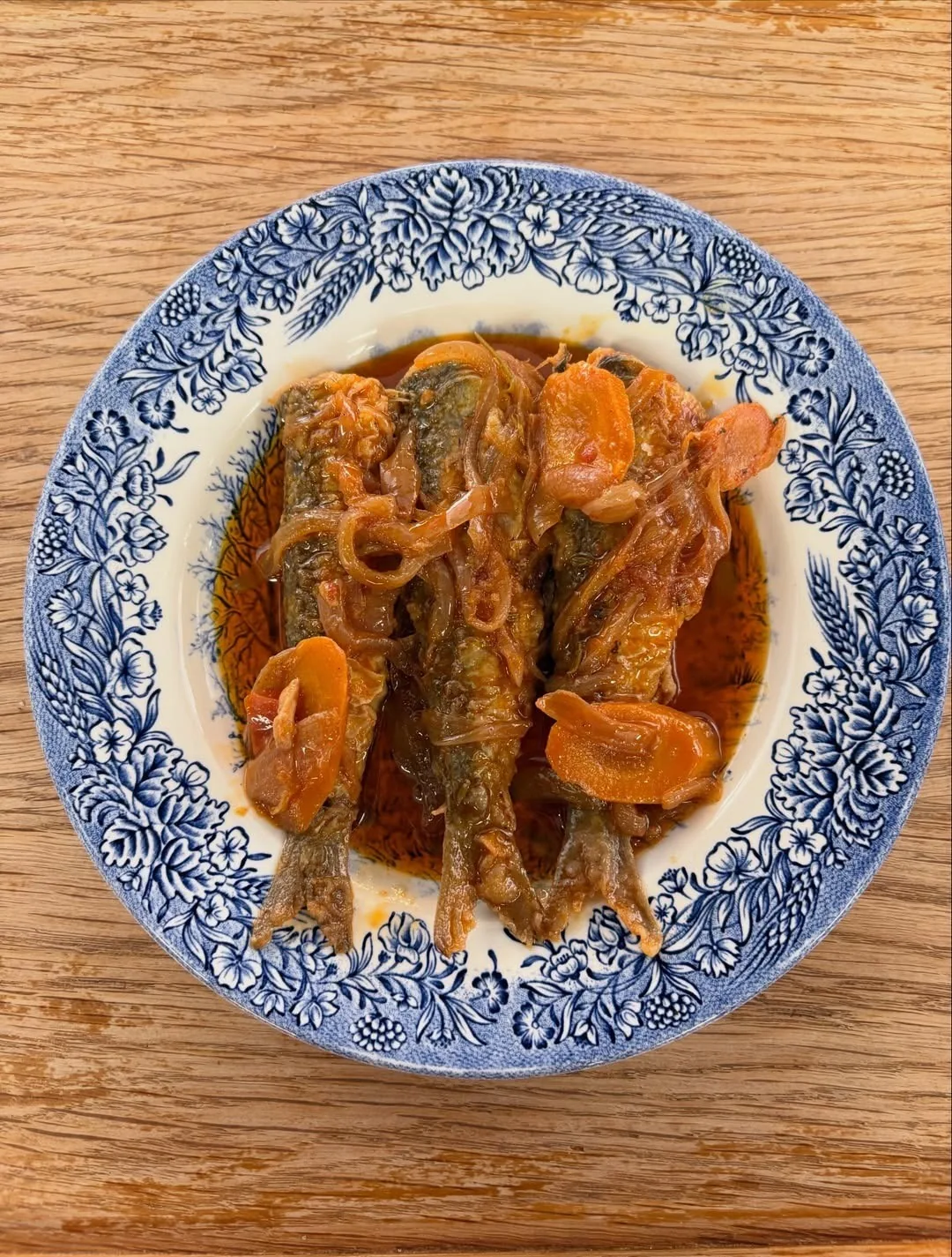A blue and white plate of small whole fish in a tomato sauce