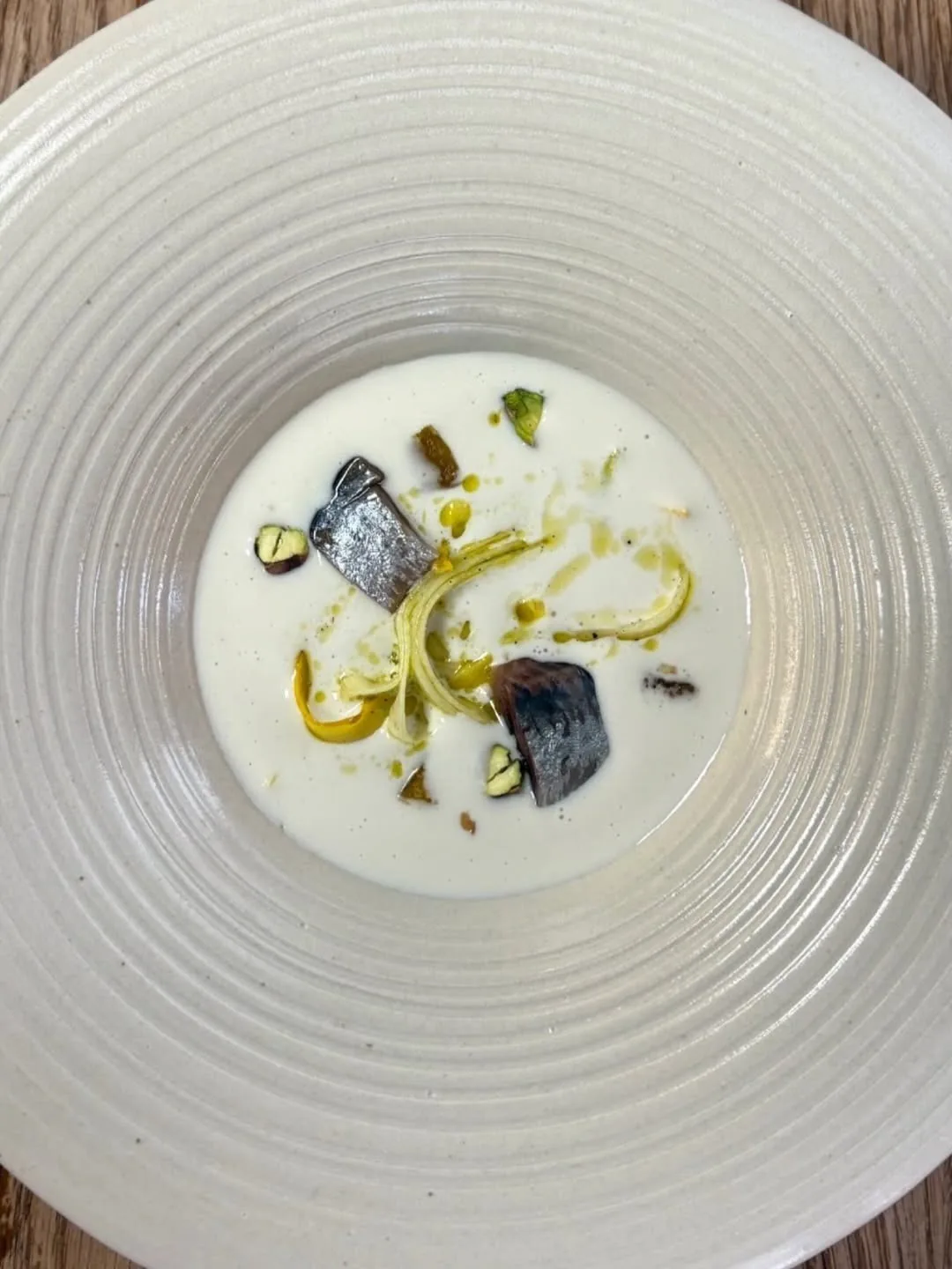 A large white bowl with a cream soup topped with two fish pieces and green herbs