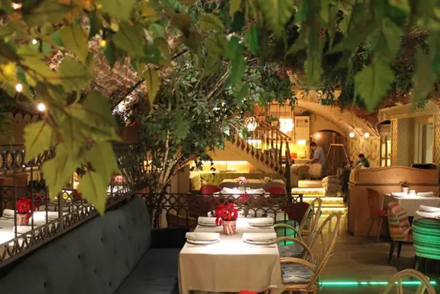 Restaurant dining room with string lights, greenery, and tables set beneath an arched ceiling.