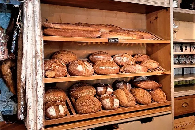 Wooden shelves stocked with loaves of bread and baguettes.