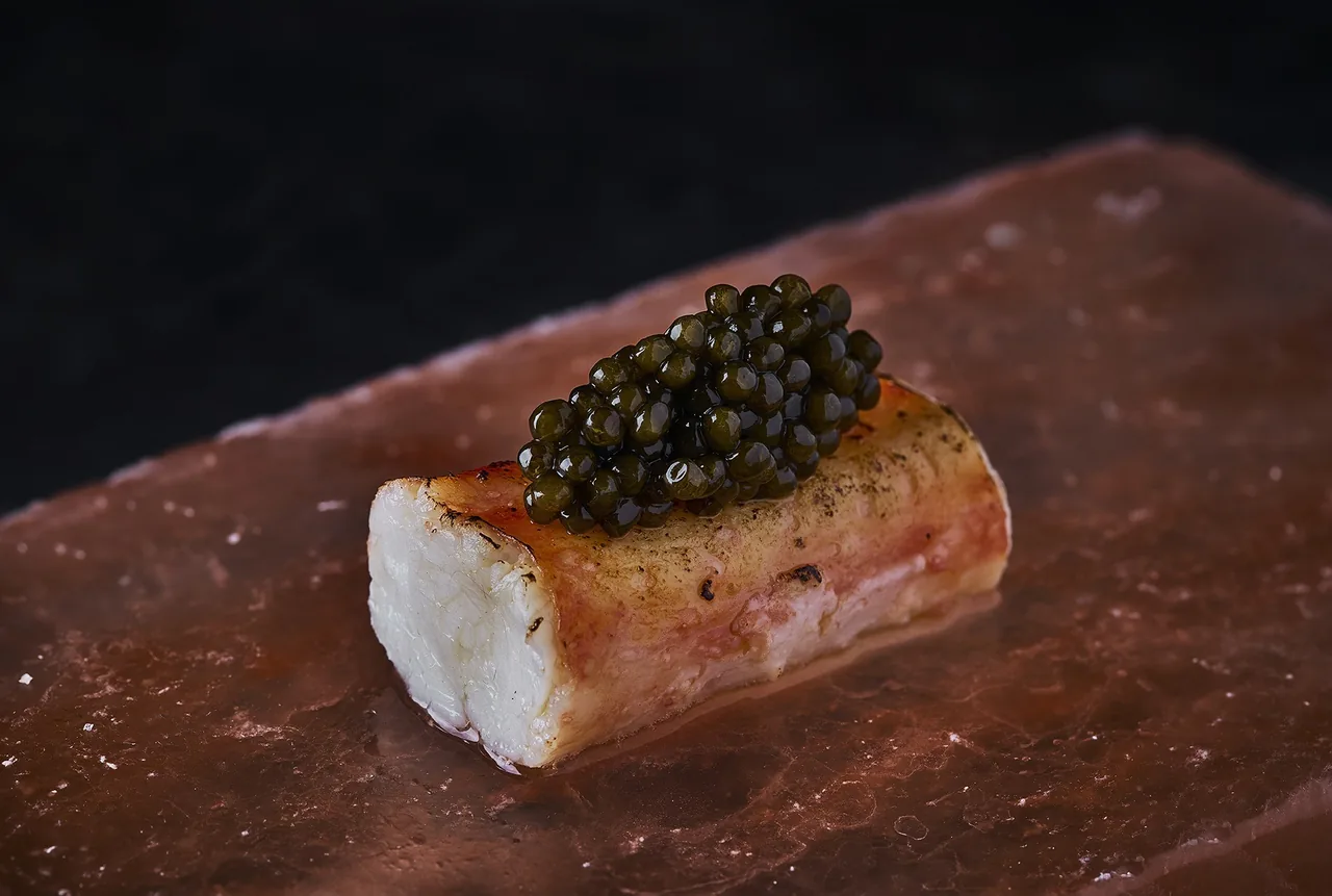 A white roll topped with dark pearls on a terracotta-coloured slab