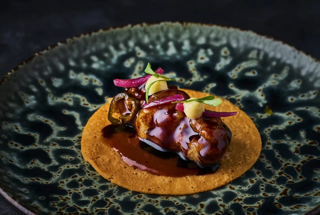 A glazed piece of food on an orange base on a dark patterned plate