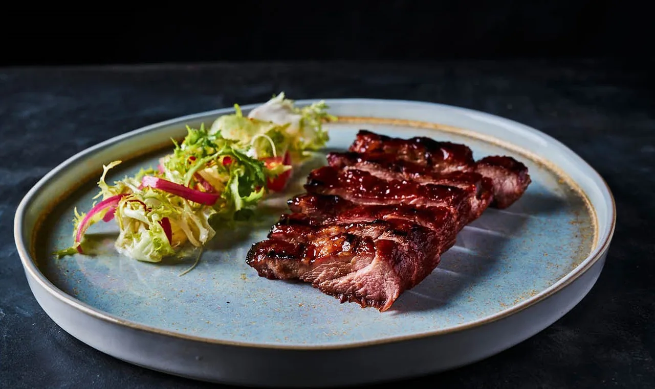 Thin slices of grilled meat and a small salad on a pale blue plate