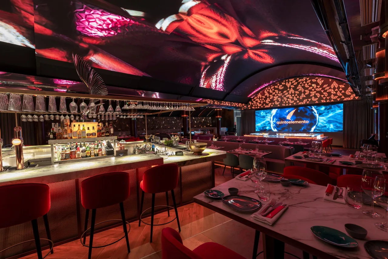 A long bar counter with red stools under a red-lit vaulted ceiling