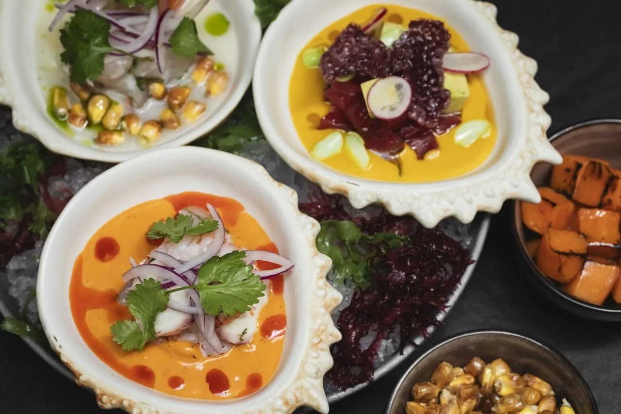 Three shells of ceviche and small bowls of side dishes on a dark tray