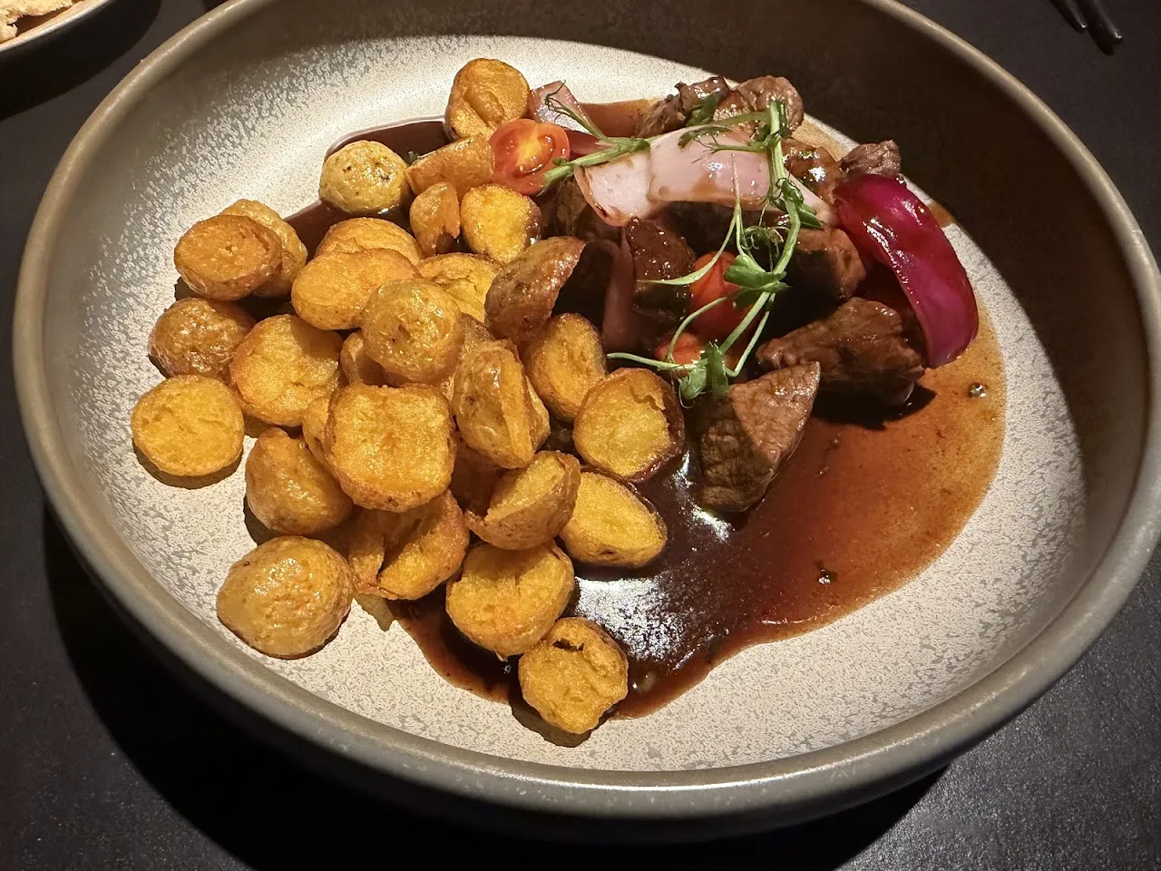 A plate of braised short rib with crispy fried plantain rounds and red onion strips