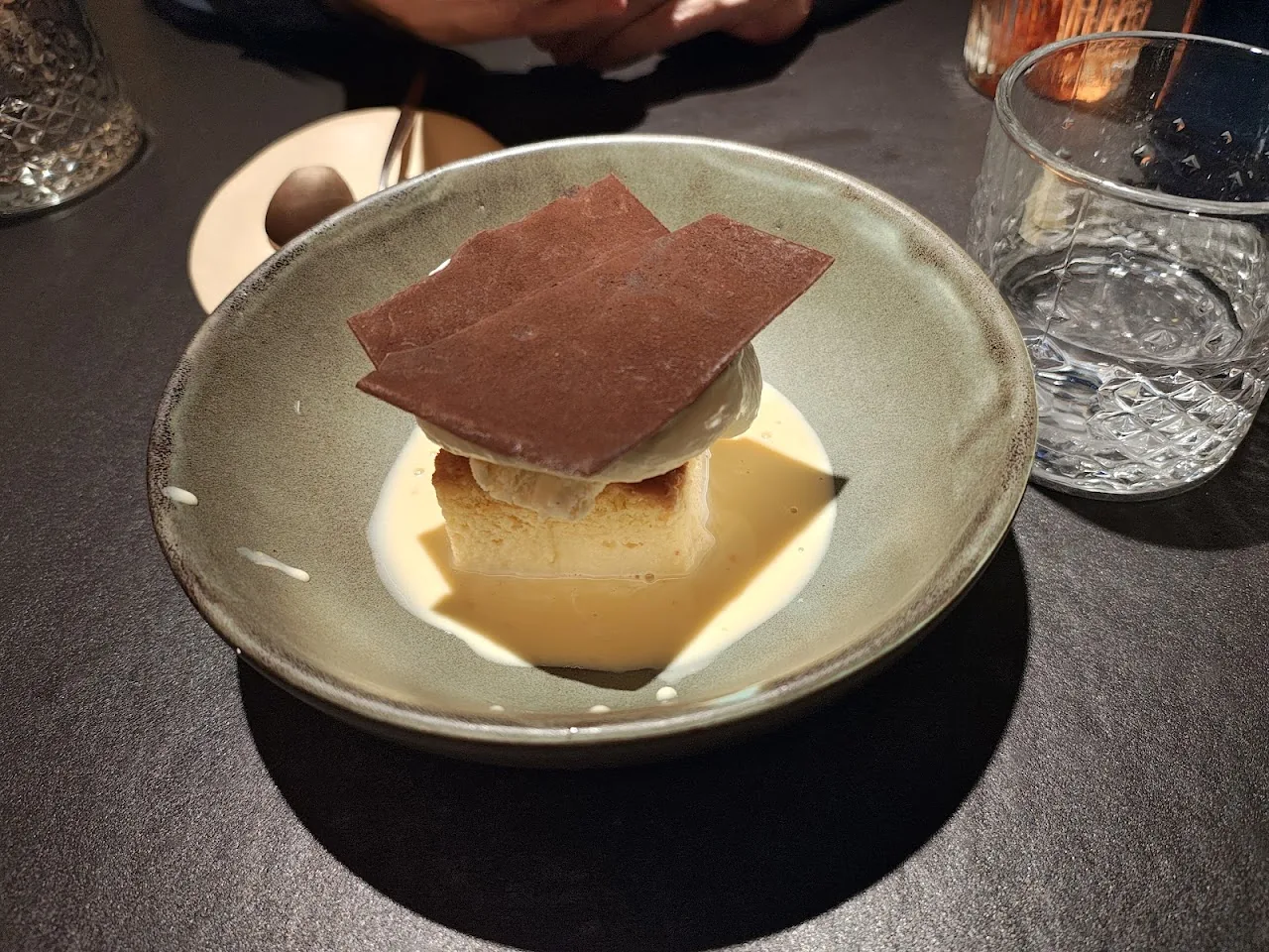 A layered dessert with a dark chocolate wafer square on top and caramel sauce pooled on the plate
