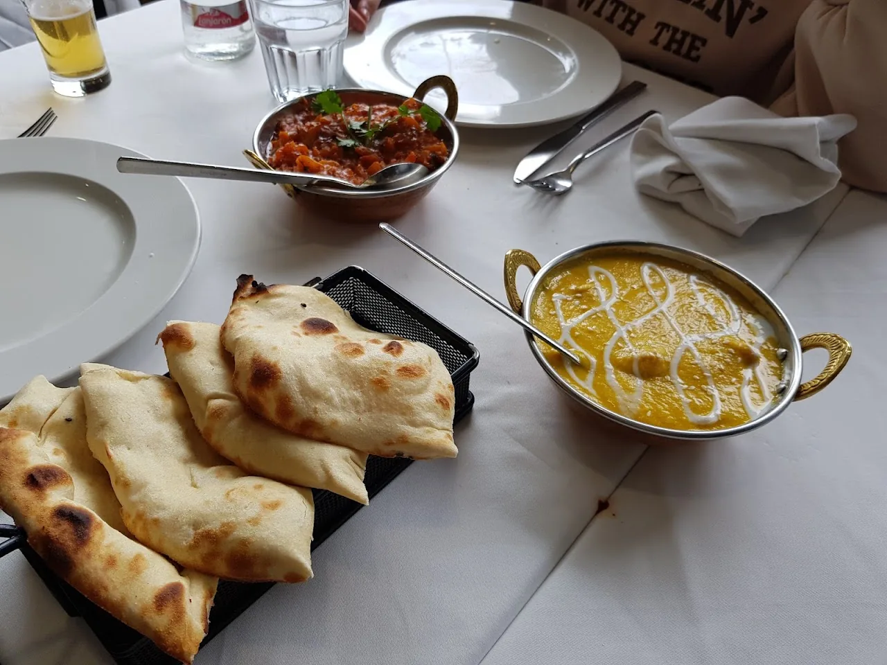Two bowls of curry served with naan bread on a table