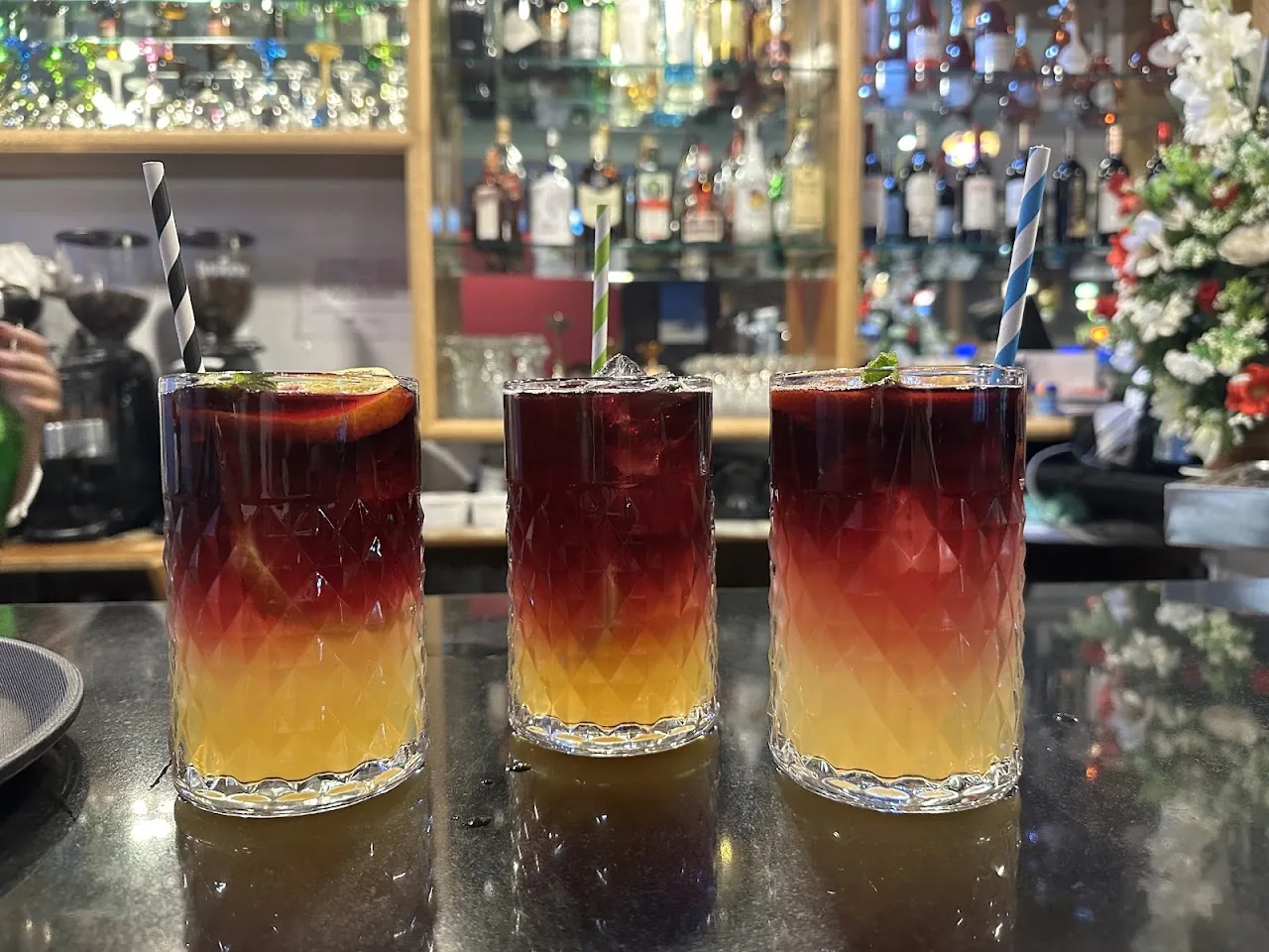Three tall glasses of red and orange layered cocktails on a bar