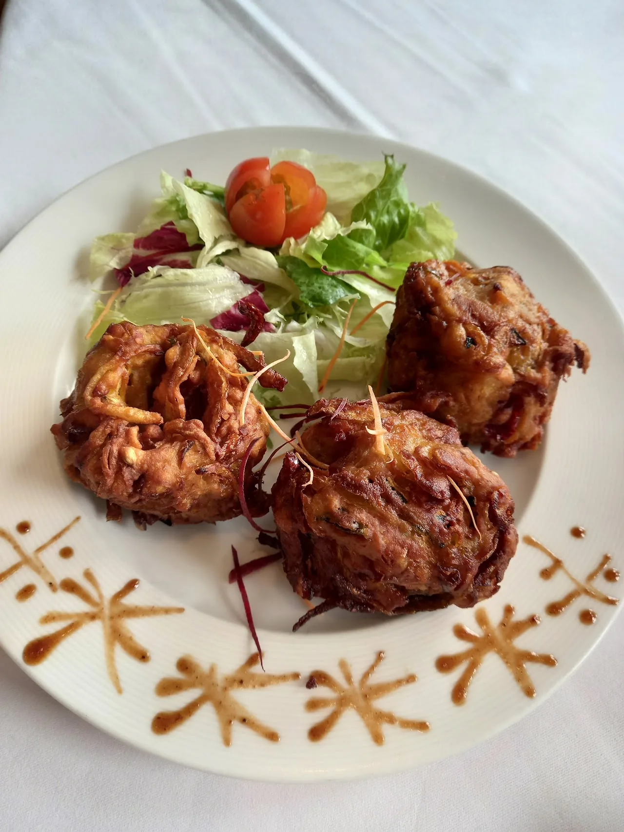 Three onion bhaji fritters plated with a drizzle of sauce