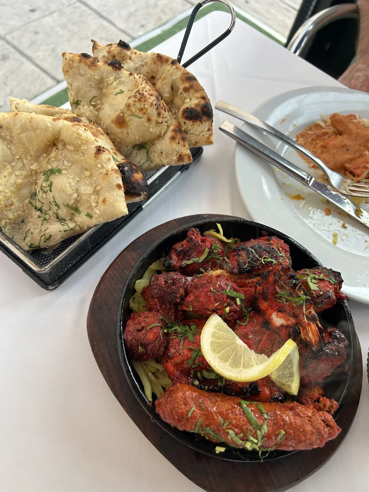 A sizzling skillet of tandoori chicken pieces served with garlic naan