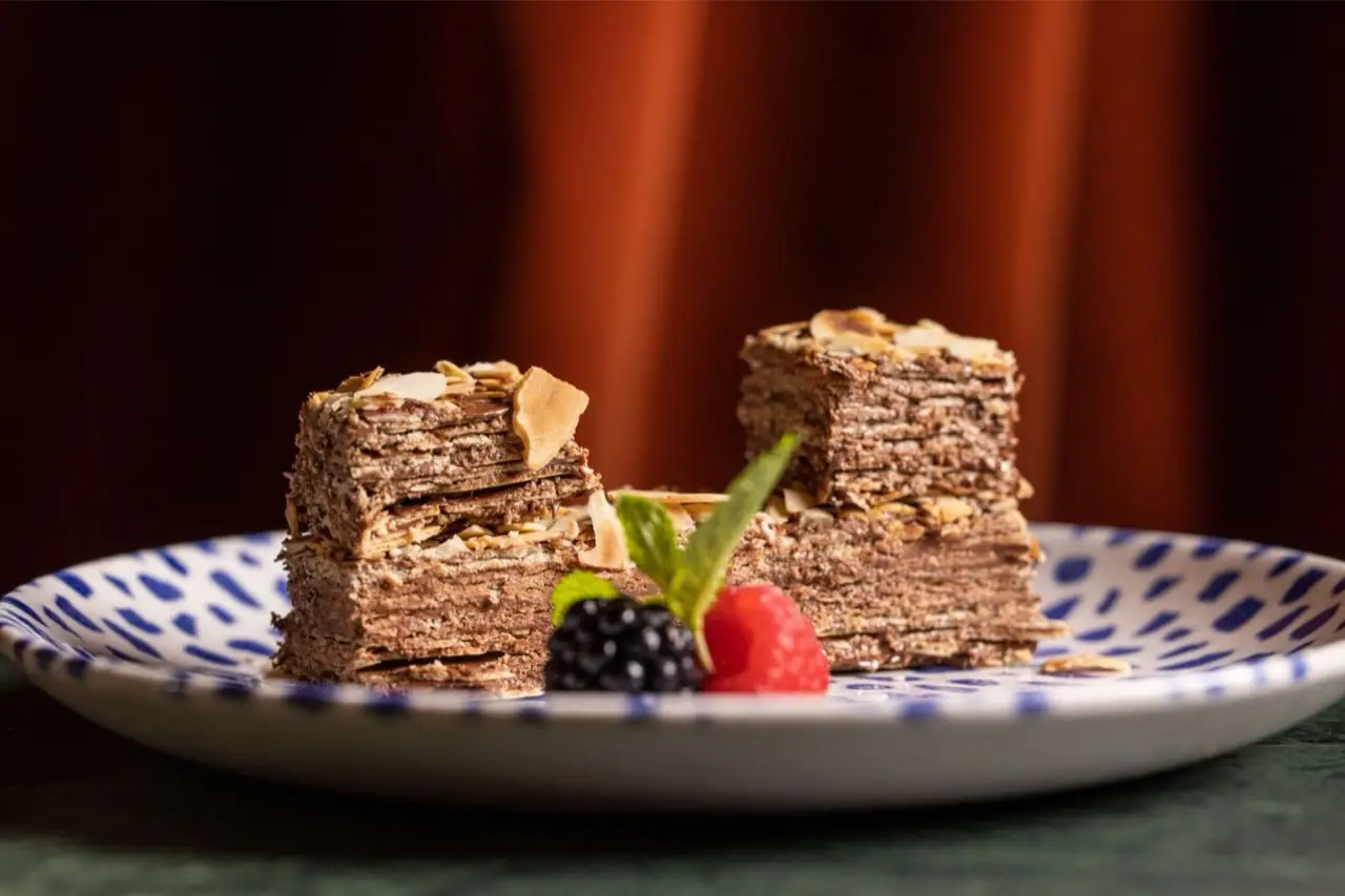 Two slices of layered chocolate-and-almond mille-feuille dessert with fresh raspberry, blackberry and mint on a blue-spotted plate