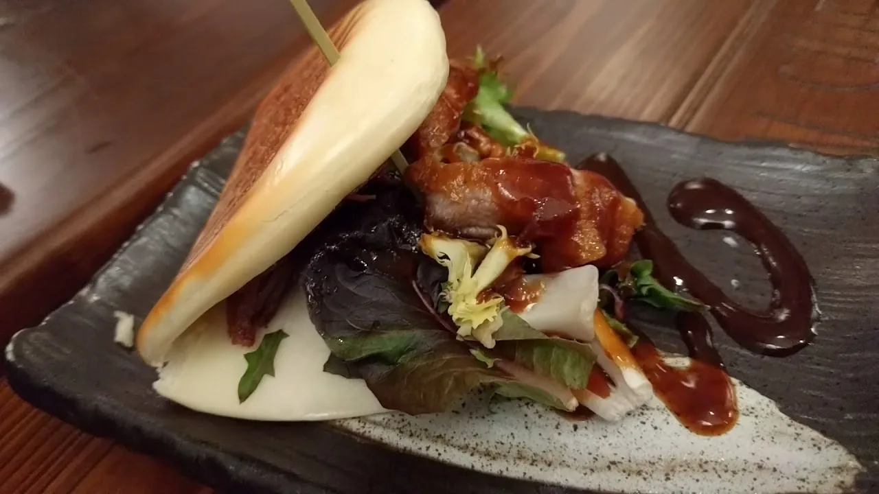 A plate of glazed pork belly with lettuce and a drizzle of dark sauce