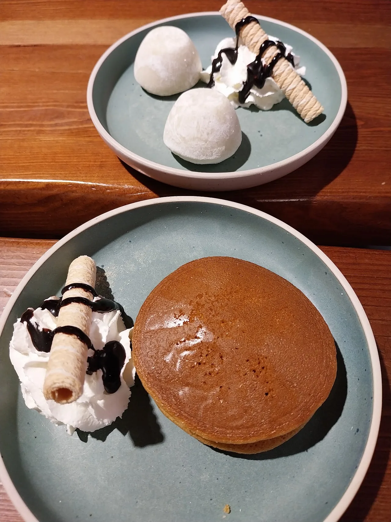 Two dessert plates with mochi-topped ice cream and a chocolate pancake drizzled with sauce