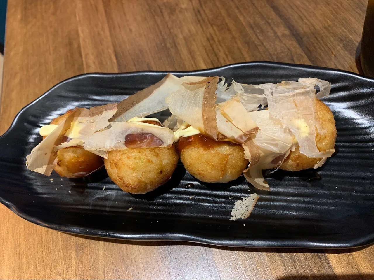 Four golden takoyaki balls topped with bonito flakes on a black dish