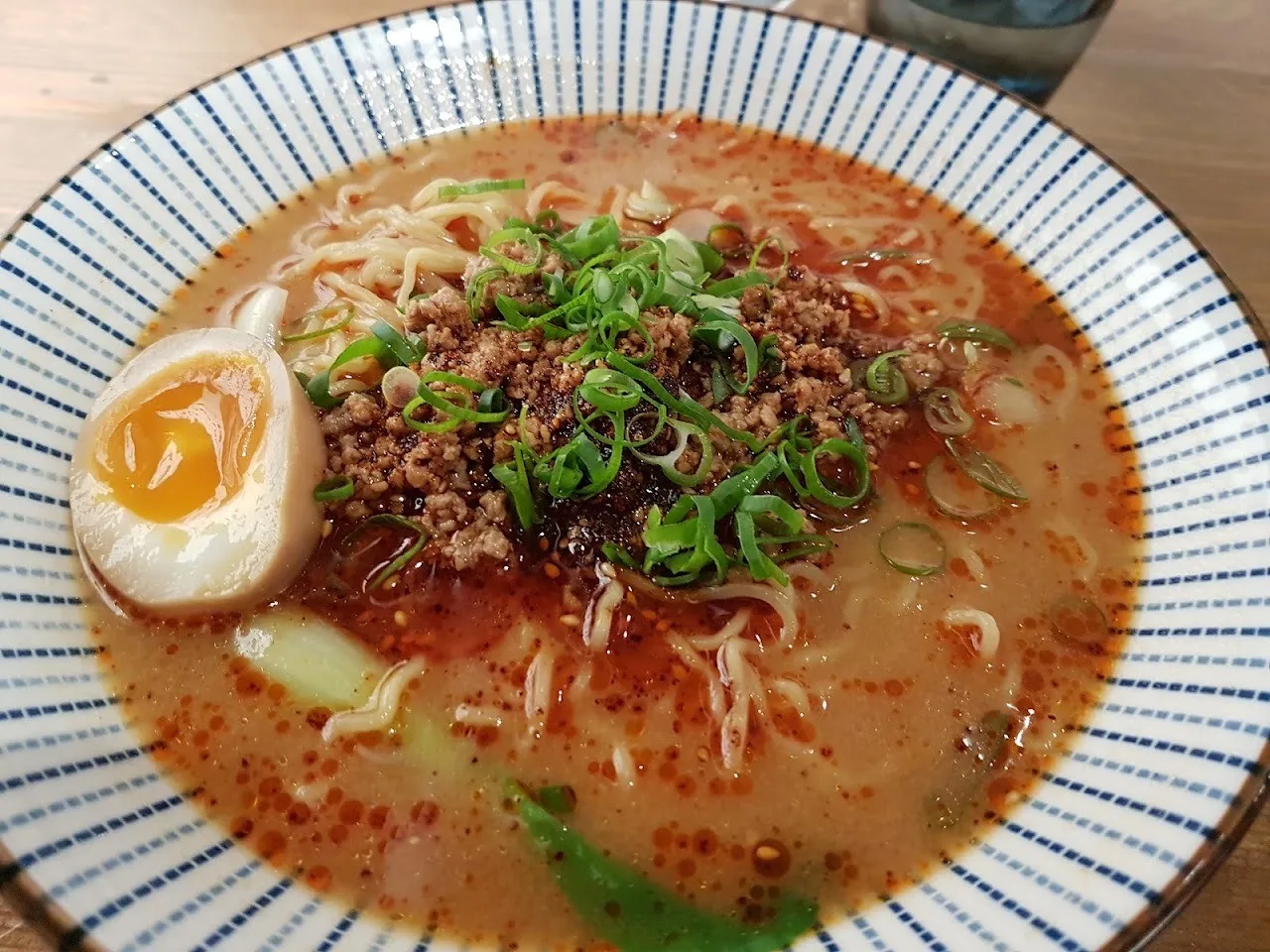 A bowl of orange ramen broth topped with minced meat, spring onion and a halved egg