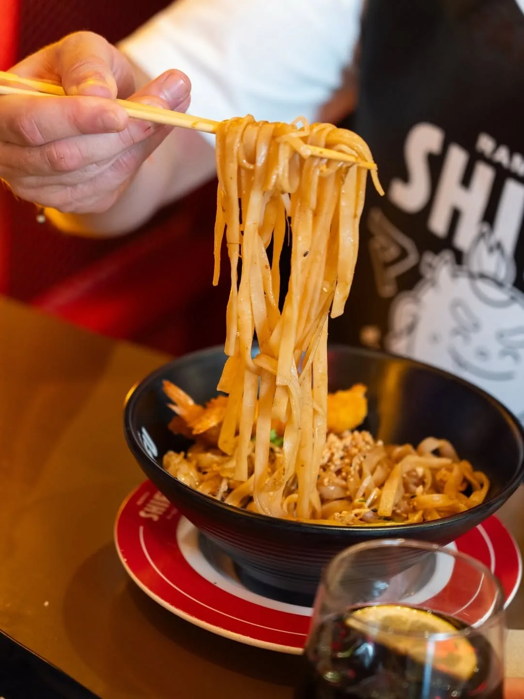 A hand lifting a bundle of noodles with chopsticks from a black bowl