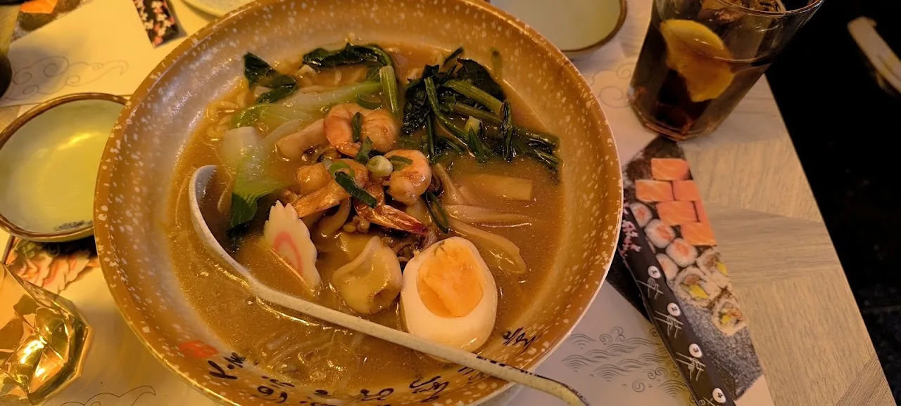 A bowl of soup with bok choy, mussels, and a halved soft-boiled egg