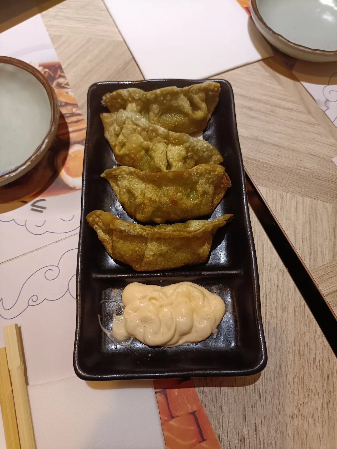 A plate of pan-fried gyoza dumplings with a dipping sauce