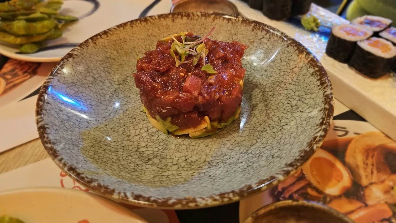 A plate of raw tuna tartare formed into a round mound, with sushi rolls in the background