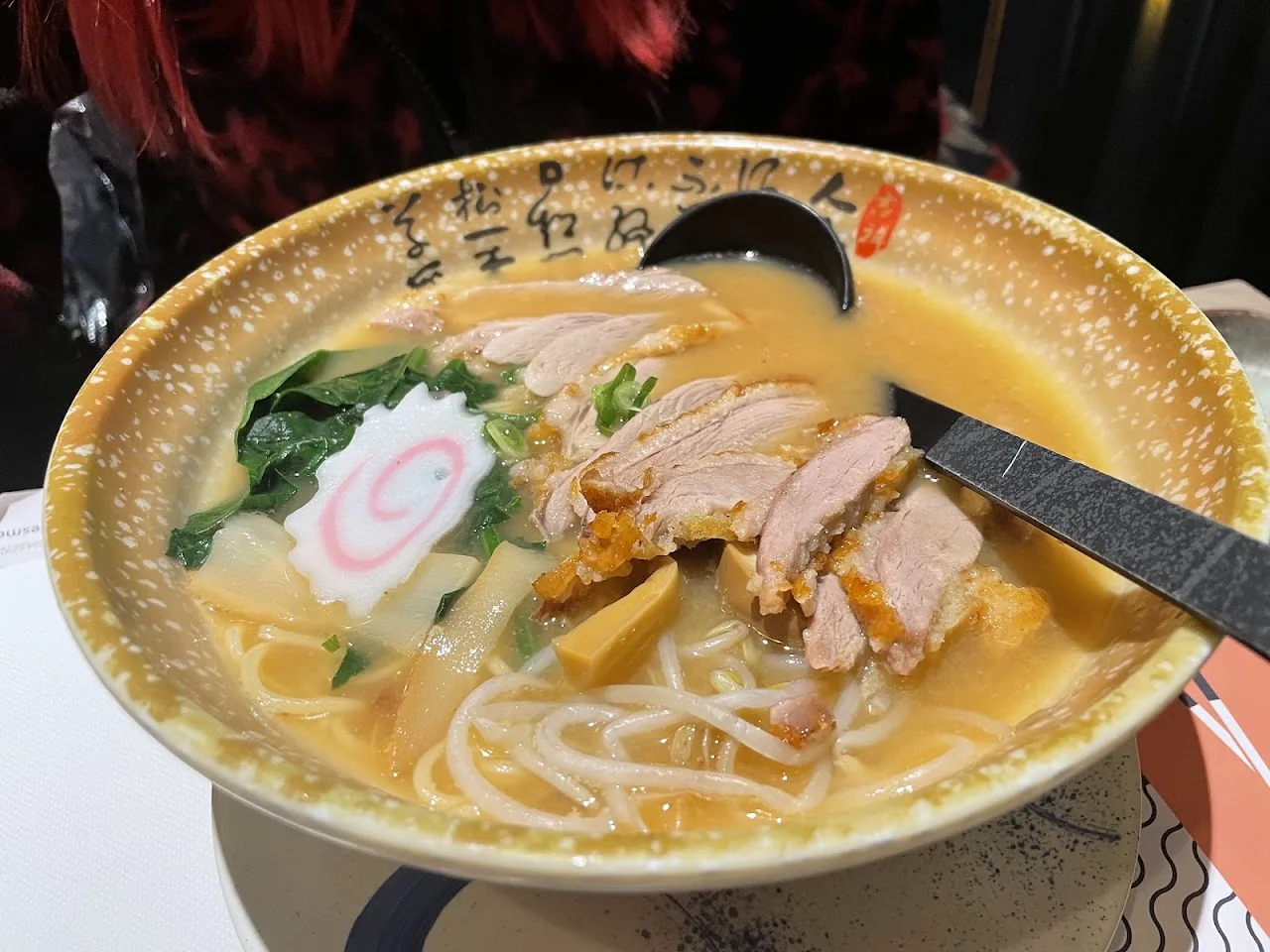 A bowl of ramen with sliced roast pork, greens, and a swirl of chili oil in a golden broth