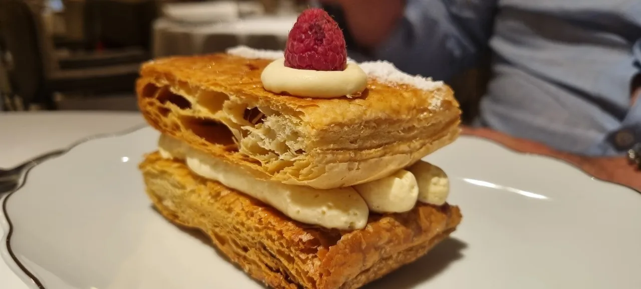 A stack of golden puff pastry layers with cream and a raspberry on top