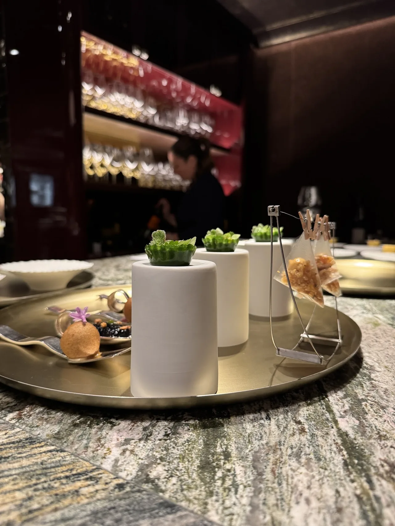 Small white cylinders topped with greenery on a metal tray on a stone counter