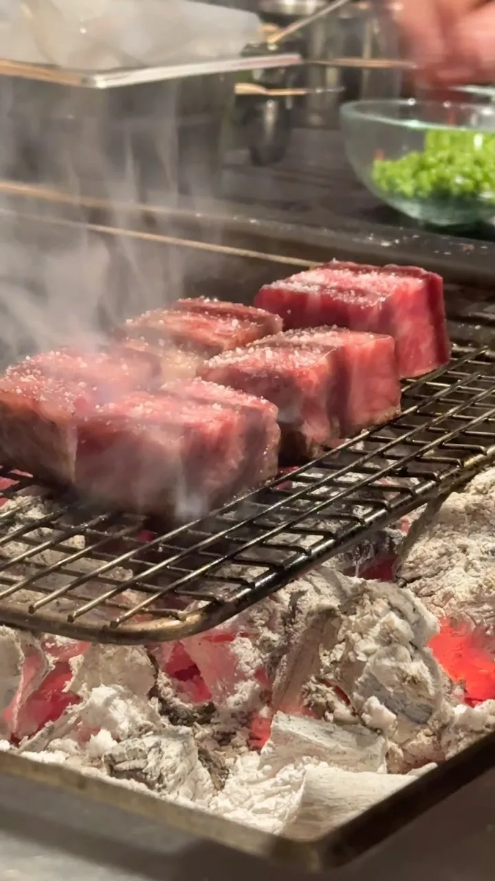 Cubes of red meat cooking over glowing coals on a grill